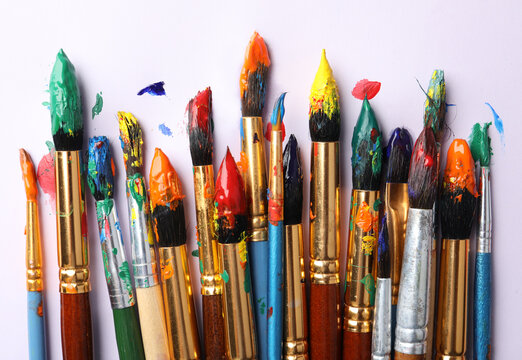 Brushes with colorful paints on white background, flat lay