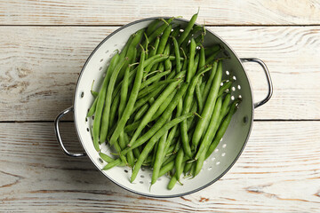 Fresh green beans in colander on white wooden table, top view