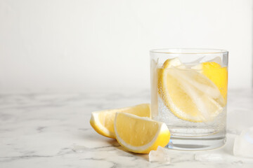 Soda water with lemon slices and ice cubes on white marble table. Space for text