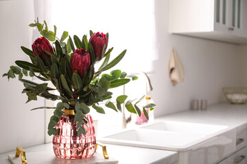 Bouquet with beautiful protea flowers on countertop in kitchen, space for text. Interior design