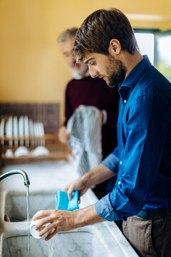 Young man washing dishes with father