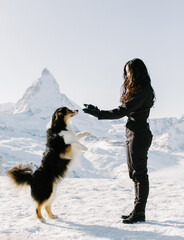 Unrecognizable girl with dark hair in black clothes stands with dog against the backdrop of a mountain landscape