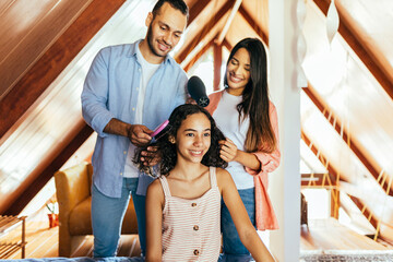 Mother and father brushing her daughter's hair at home.