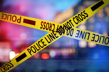 Yellow law enforcement tape isolating crime scene. Blurred view of city, toned in red and blue...