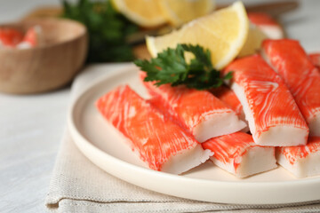 Plate of fresh crab sticks with lemon on white table, closeup
