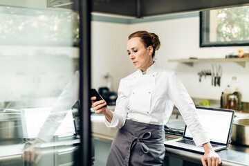 Female chef using smartphone near laptop