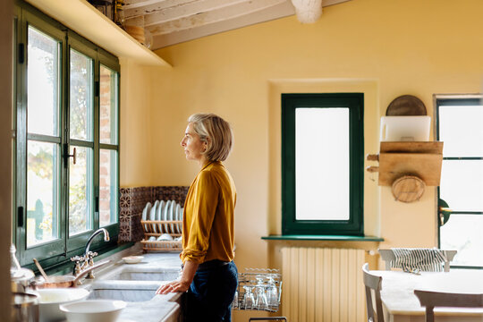 Dreamy woman looking out window in kitchen
