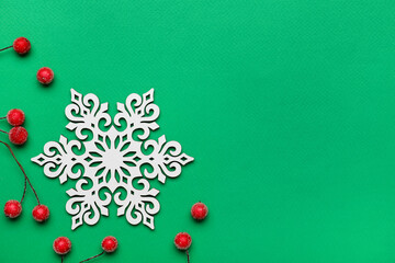 Beautiful decorative snowflake and red berries on green background, flat lay. Space for text