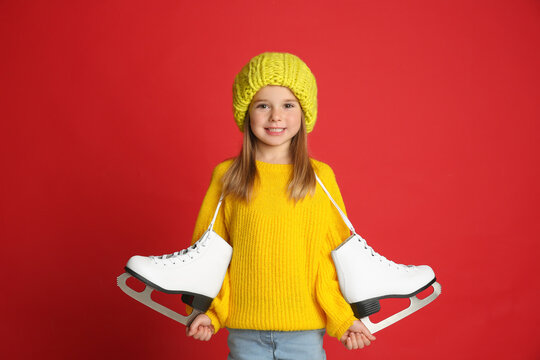 Cute little girl in yellow knitted sweater with skates on red background