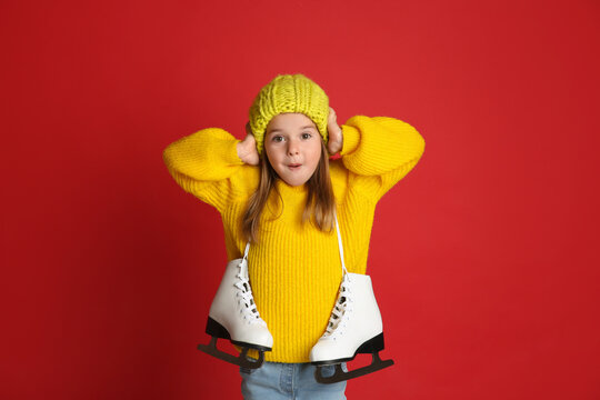 Excited little girl in yellow knitted sweater with skates on red background