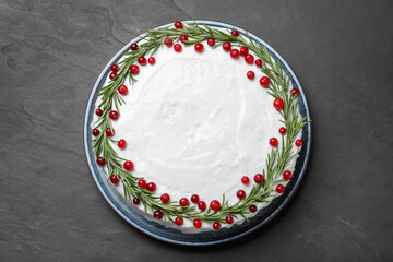 Traditional Christmas cake decorated with rosemary and cranberries on dark grey table, top view