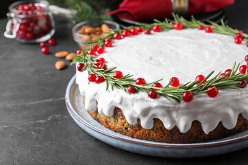 Traditional Christmas cake decorated with rosemary and cranberries on dark grey table, closeup