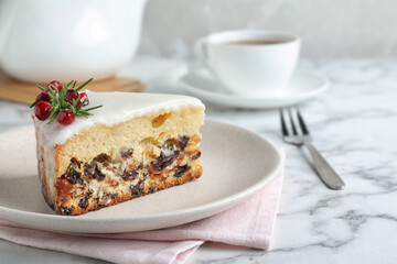 Slice of traditional Christmas cake decorated with rosemary and pomegranate seeds on white marble table