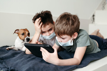 Young brothers in protective medical masks at the game tablet.