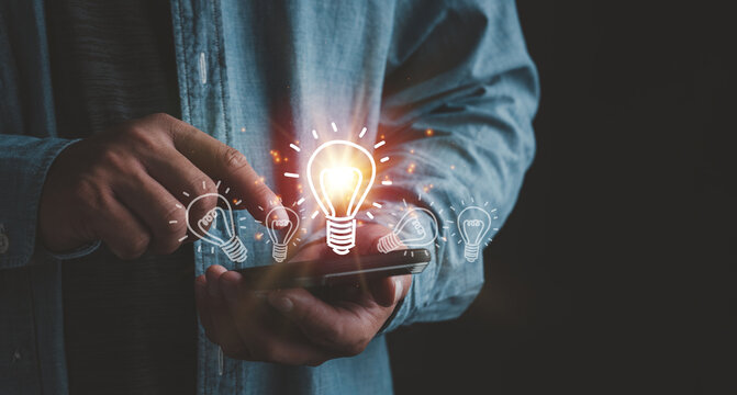 Businessman touching smartphone with light bulbs on the phone screen. ideas of new ideas with innovative technology and creativity.