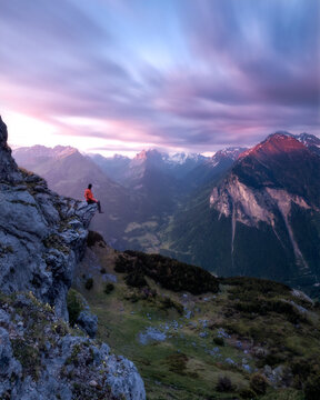 Man sitting on a cliff overlooking the alps and a dreamy sky