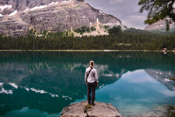 Woman standing on rock by turquoise alpine lake O'Hara in Yoho National Park. British Columbia. Canada 
