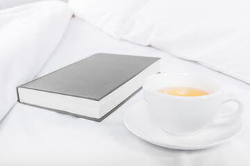 Tea and book on the bed. White sheets and grey book. White background. Copy Space.