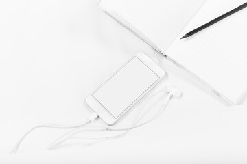 Notebook, pencil, Smartphone, and earphones, on the bed, white sheets. White background, copy space, mockup.