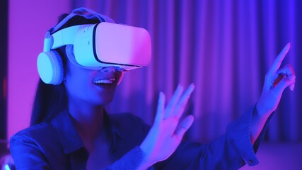 Young asian woman is using virtual reality headset. Neon light studio portrait. Concept of virtual reality, simulation, gaming and future technology.Asian woman play game in bedroom.