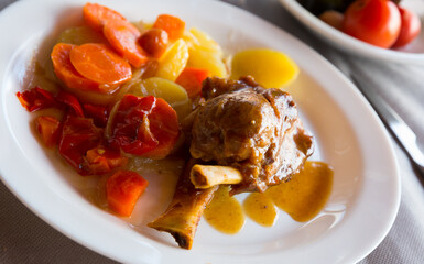 Appetizing baked pork knuckle (Codillo) with baked potatoes and carrot on plate