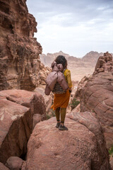 A tourist girl in a yellow shirt and a backpack stands on a rock and prepares to go down