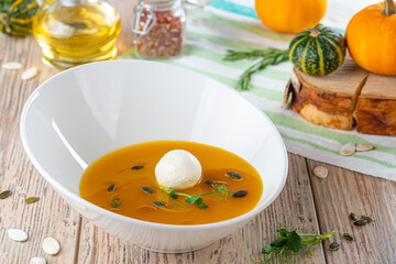 bowl with pumpkin cream soup and cheese on wooden background, close view, autumn and vegetarian concept 