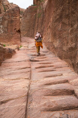 a tourist girl with a backpack walks along the steps of the ancient city carved out of stone