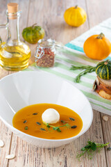 bowl with pumpkin cream soup and cheese on wooden background, close view, autumn and vegetarian concept 