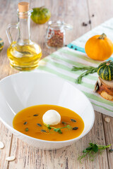 bowl with pumpkin cream soup and cheese on wooden background, close view, autumn and vegetarian concept 