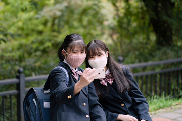 スマートフォンを見るマスクをつけた女子学生2人