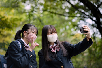 スマートフォンで自撮りをするマスクをつけた女子学生2人