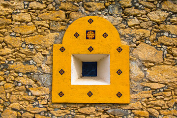Pequeña ventana amarilla en muro de piedra con marco decorativo casa rustica desértica
