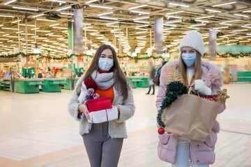 Fototapeta na wymiar Young women in medical mask shopping for Christmas in mall. Xmas holidays in new Covid-19 reality.