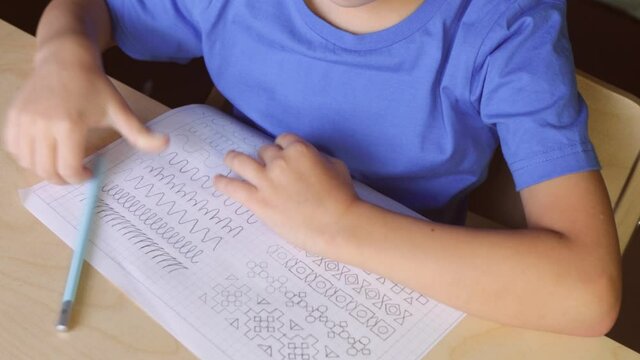 Child boy writing different lines with pencil. Prewriting practice to prepare hands for write letters. Children education concept. View from above