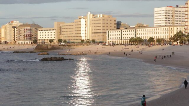 riazor beach in A Coru&ntilde;a, Spain with people walking and bathing at sunset