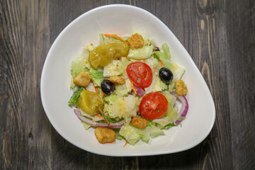 Top view of a ceasar salad with tomatoes, purple onion, black olives, pepperoncini peppers and croutons.