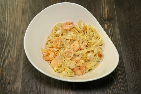 A white bowl with Alfredo fettuccine pasta with shrimp and scallops.