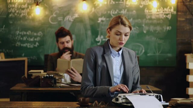 Professor and secretary or assistant working at his desk with vintage typewriter front of a blackboard.