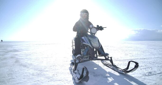 Young asian woman riding a snowmobile vehicle on the frozen Lake Baikal in winter with happy emotion. Extreme Sport Activity and Recreation in Cold Season. 
