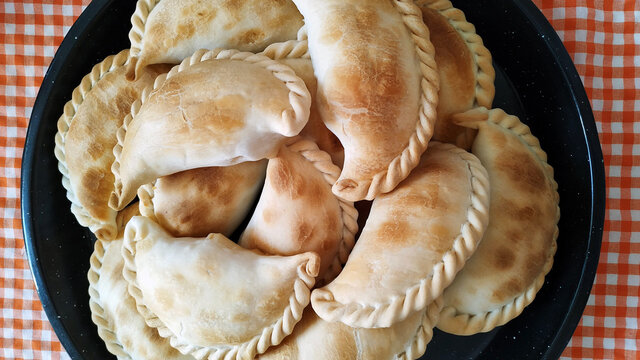 Fuente de empanadas caseras tradicionales argentinas sobre un mantel de estampado a cuadros naranja.