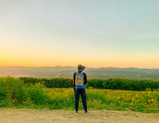 Young man asian traveler looking view sunset on Tung Bua Tong, Mae Moh, Lampang, Thailand. Mexican sunflower field. Travel concept