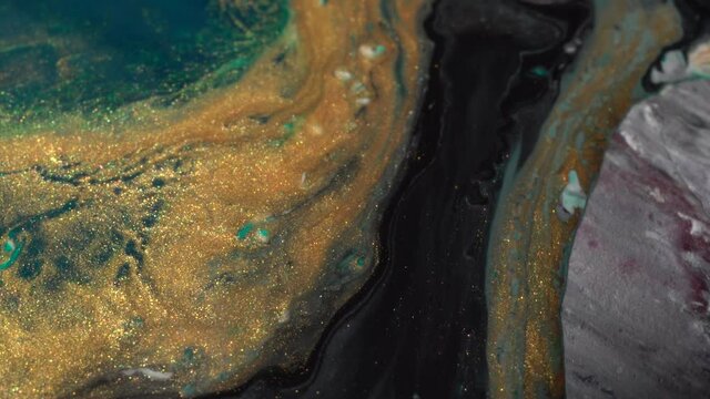 Green, white and shiny gold colors oil paint pouring close up. Fluid Art painting. Paint movement macro. Ink flow. Glitter fluid motion. Moving flowing stream of paint. Abstract background
