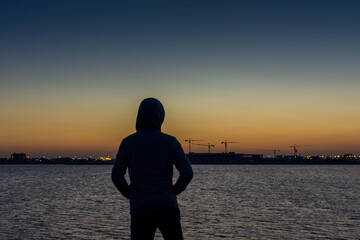Fototapeta premium A man wearing jacket with hat watching sun rising from sea at the corniche park in Dammam, Kingdom Saudi Arabia