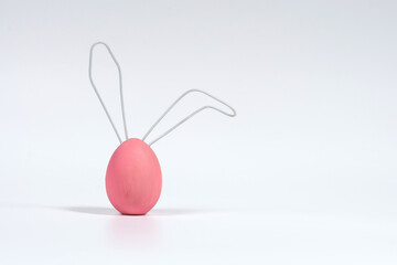 Pink Easter egg with ears made of wire. The concept of the Easter Bunny. White isolated background with soft shadow, close-up.