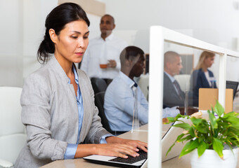 Portrait of focused asian woman entrepreneur working with laptop in busy open plan office