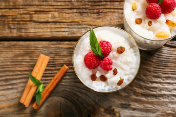 Glass cups of tasty rice pudding with raspberry and raisins on wooden table