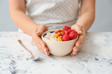 Woman holding bowl of tasty rice pudding with raspberry and nuts on white table