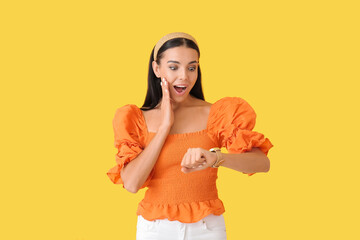 Surprised young woman with wristwatch on color background