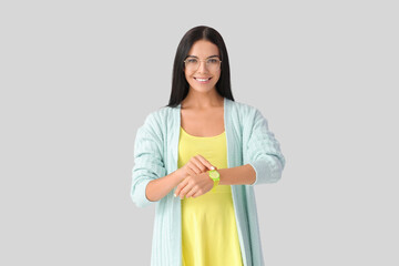 Young woman with wristwatch on grey background